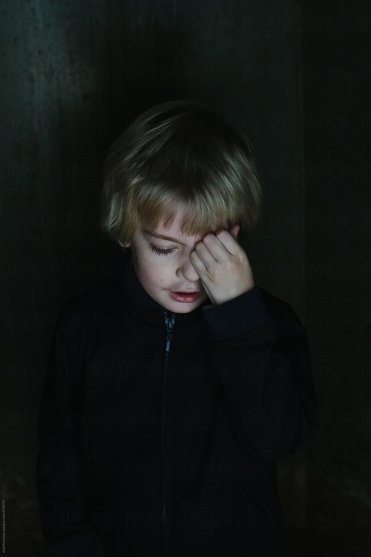 Low light, painterly image of a young boy rubbing his eye.
