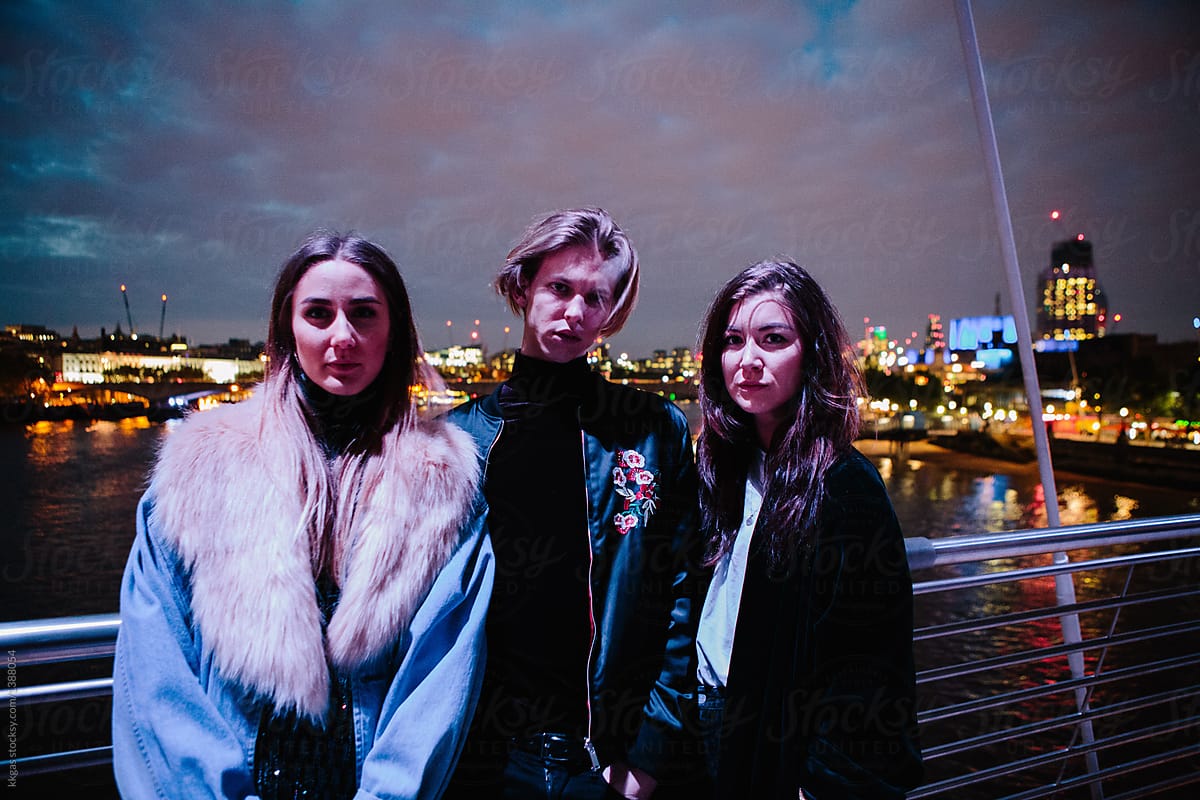 Three friends stand in front of London at night