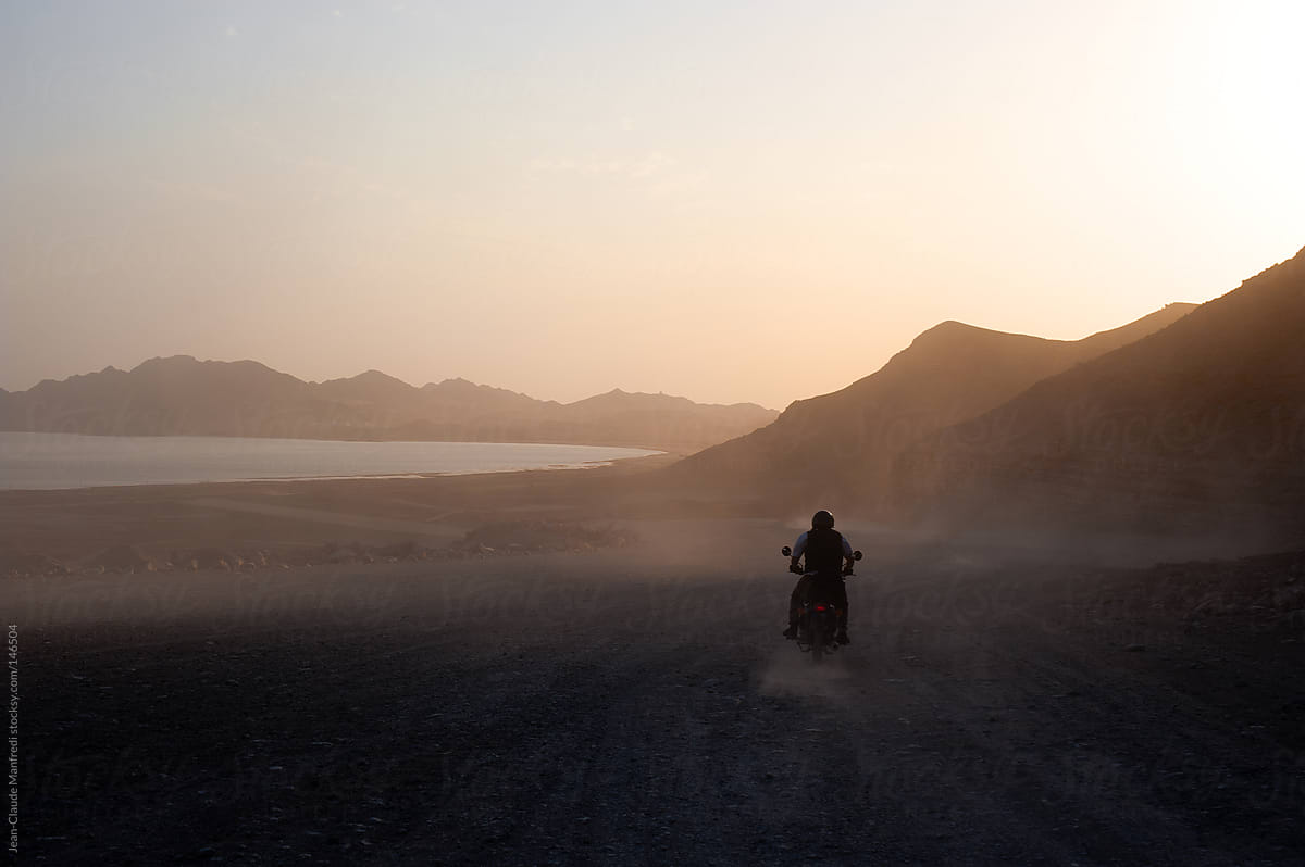 Motorcyclist rides his bike on a dirt and wild road at sunset towards the Caspian Sea