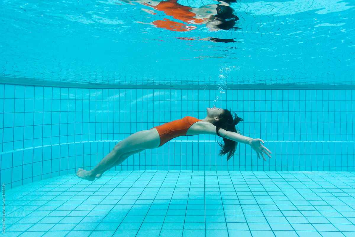 A woman in a red swimsuit is diving underwater in a pool.