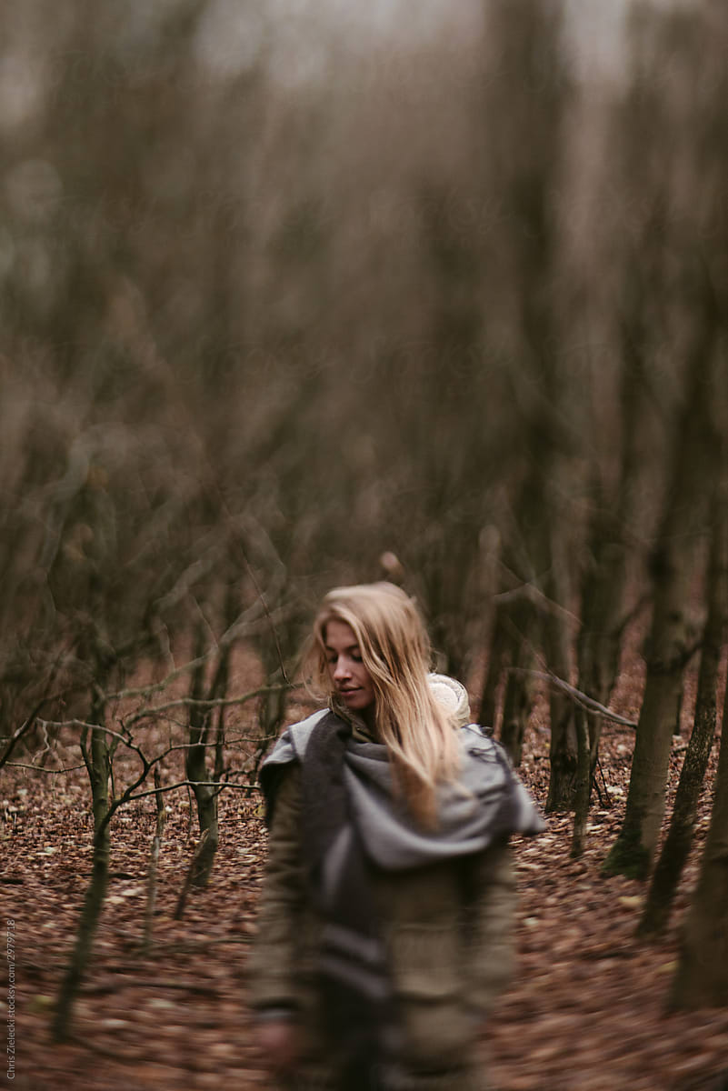 Woman wrapped in scarf standing in leafless forest
