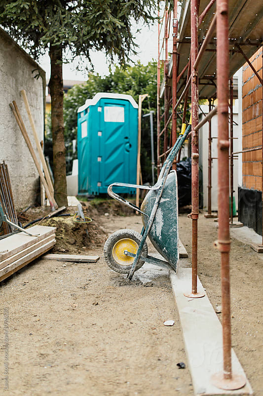 Dirty wheelbarrow leans against iron scaffolding on building site