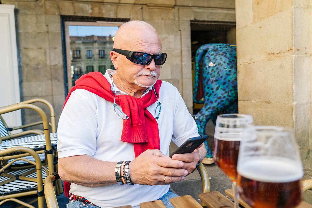 Senior man browsing smartphone in outdoor cafe