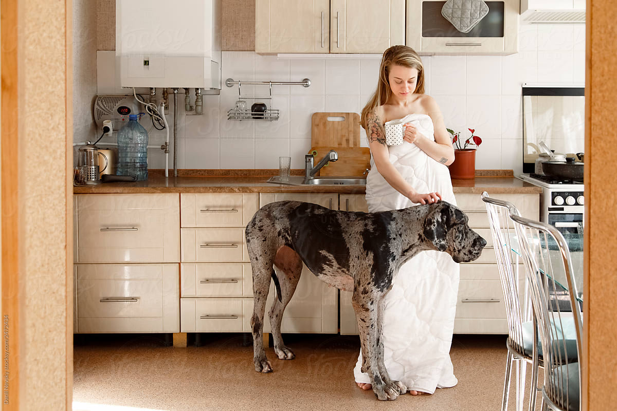 Woman with mug scratching head of dog in morning