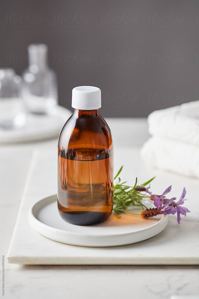 Brown glass bottle with lavender flower on plate.