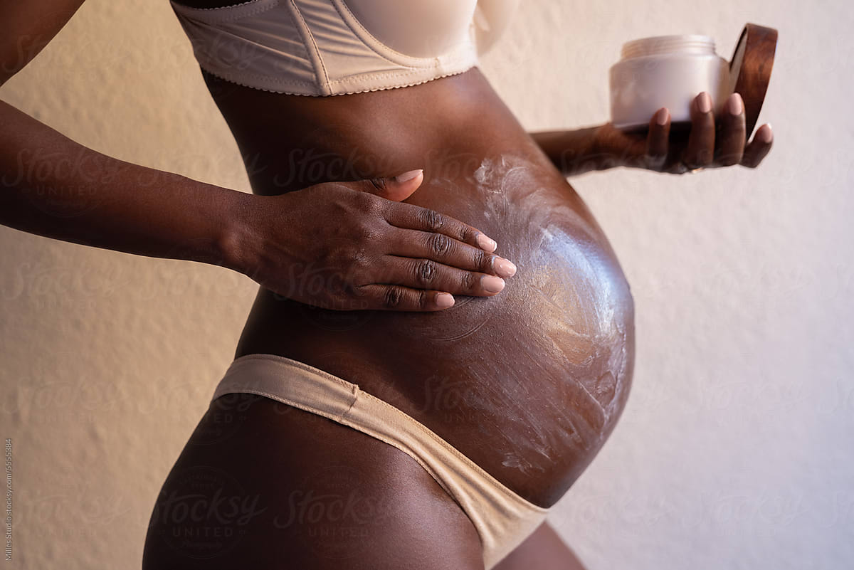 Crop female with baby bump applying belly butter