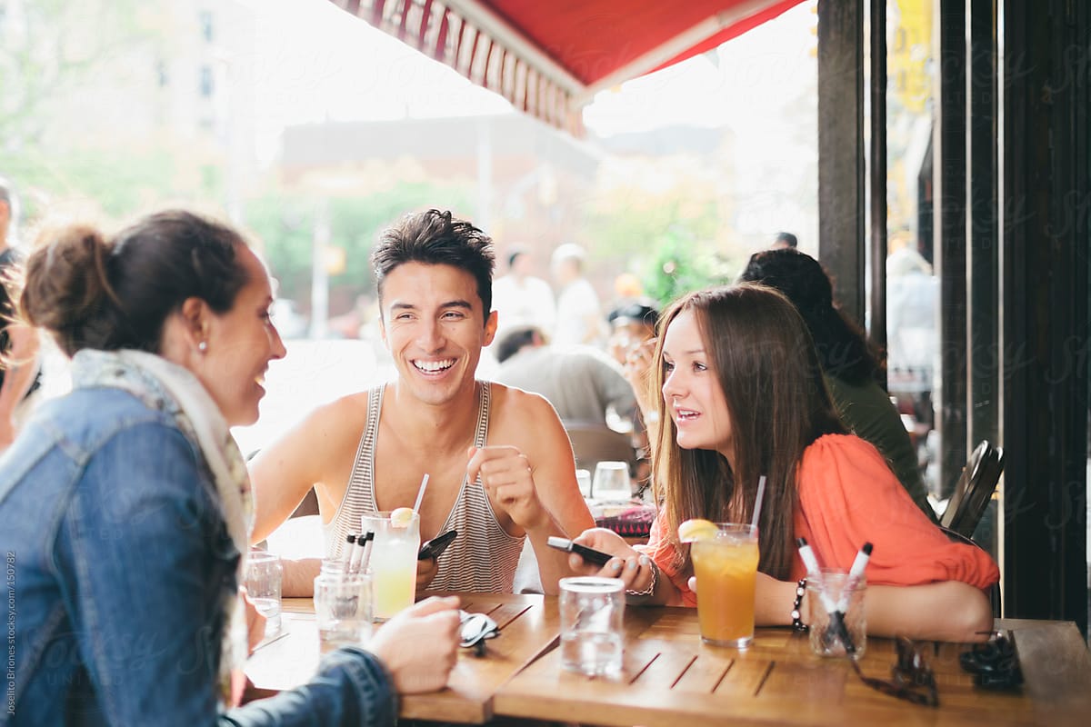 Three Friends Having Fun In Outdoor Cafe With Their Cellphones Del Colaborador De Stocksy 
