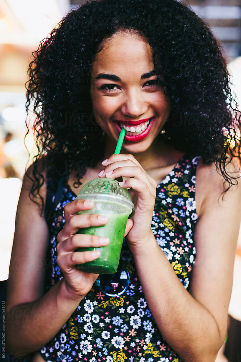 Portrait of a happy latin woman drinking a fresh smoothie standing on a marketplace.