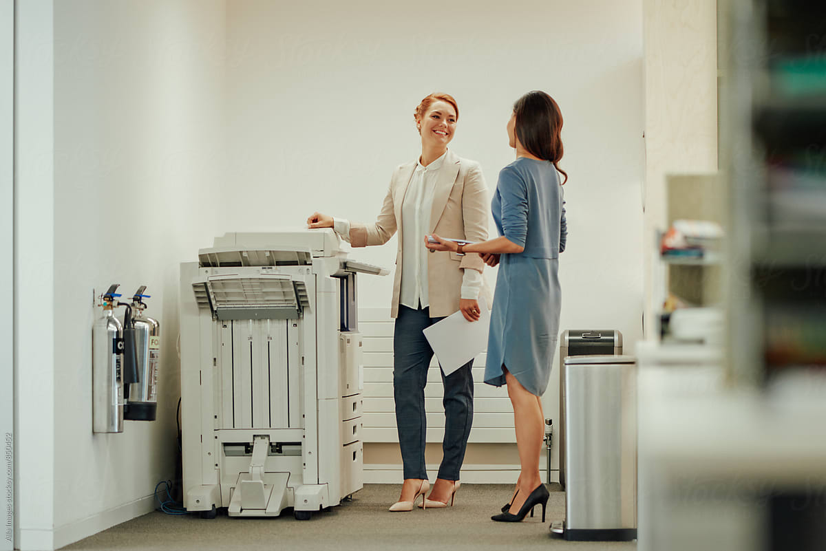 Two young business women interacting next to office photocopier