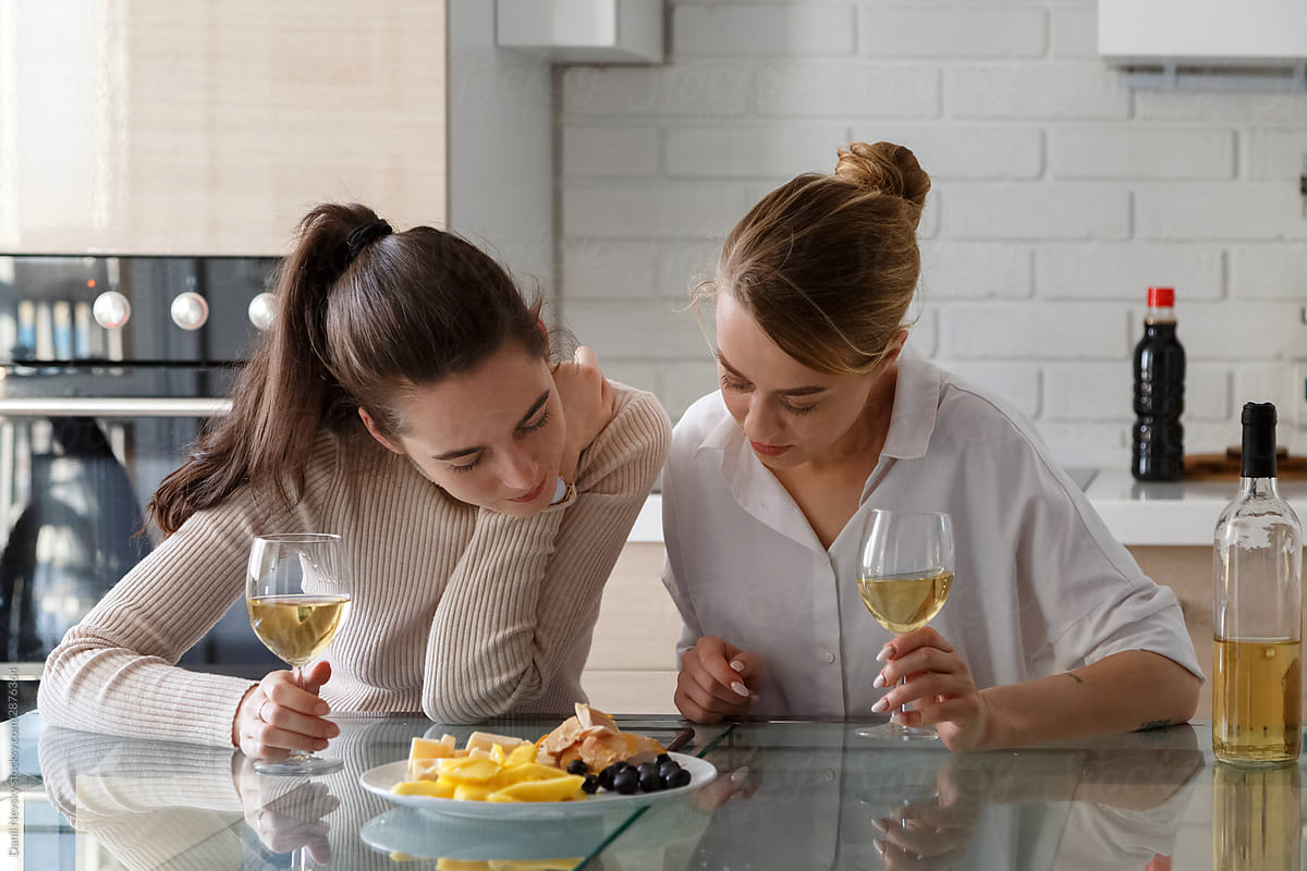 Charming women with glass of wine browsing smartphone in kitchen