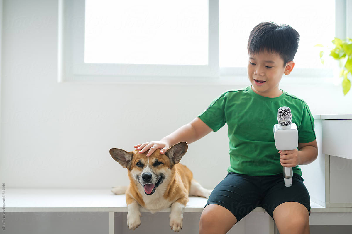 Happy boy singing karaoke with corgi dog near window