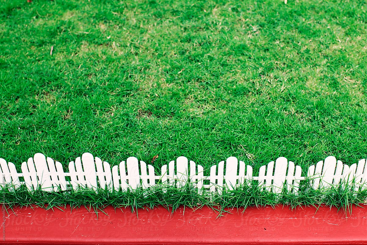 Green lawn with white picket fencing and red pavement