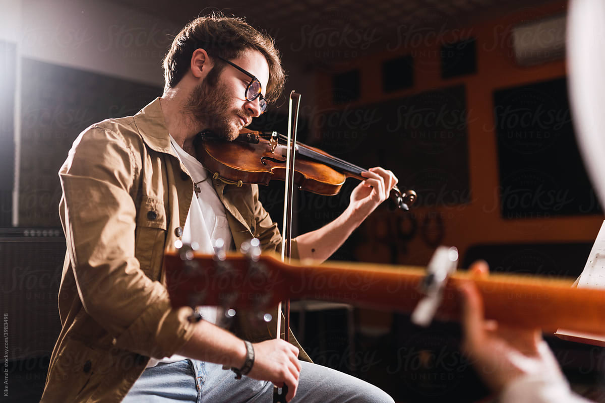 Man playing on violin near person with guitar in studio