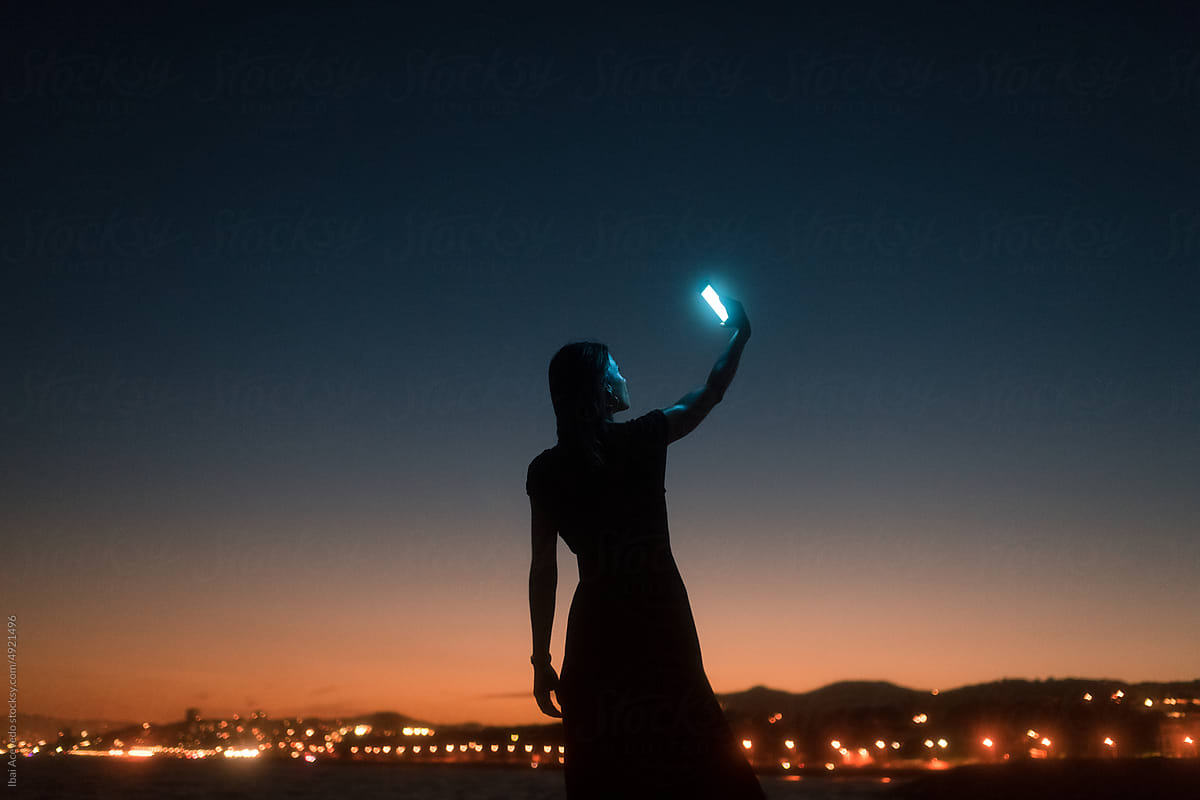 Surreal woman silhouette holding up luminous phone