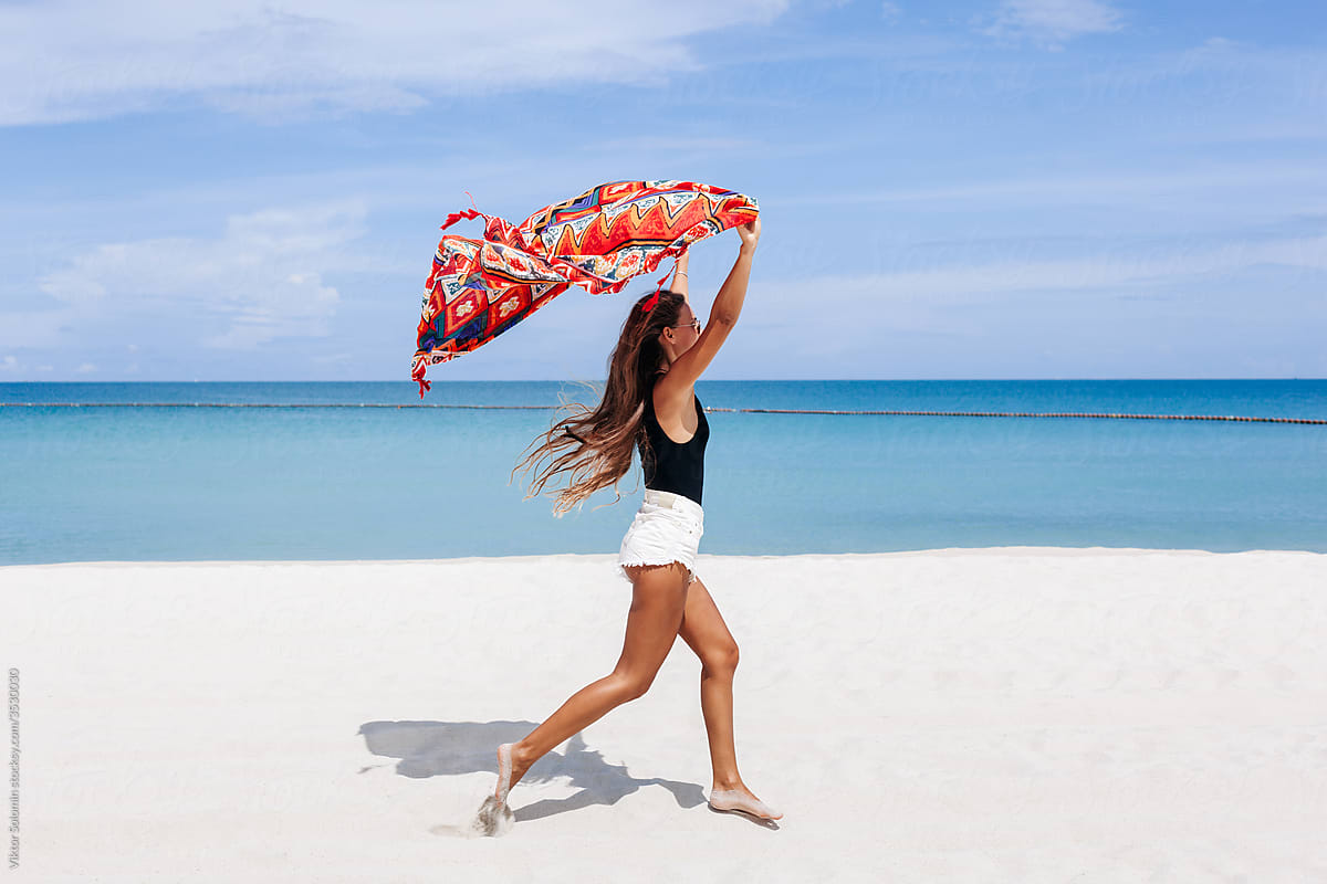 Carefree woman running along beach with fluttering scarf