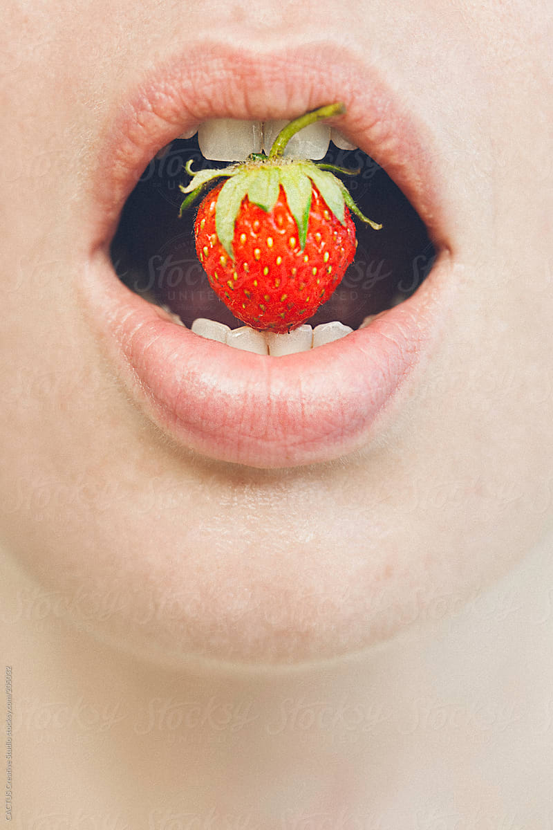 Woman showing a strawberry between her teeth