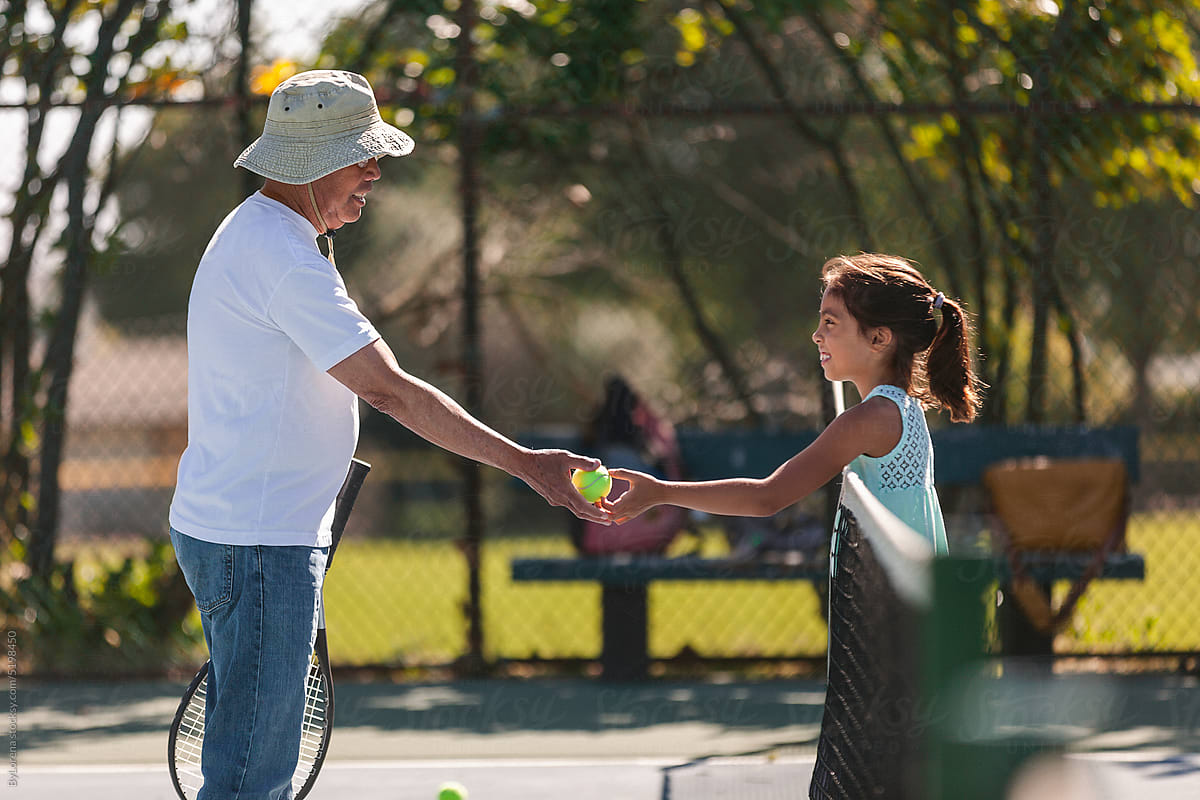 Senior man playing tennis with granddaughter outdoor