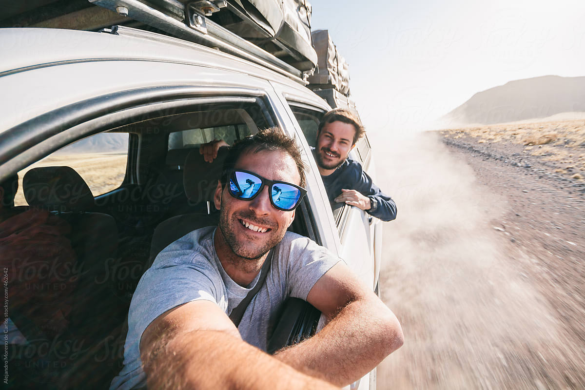 Adventure travel - Two young men taking a self portrait through the window of an off-road car while driving on a dirt road during a road trip