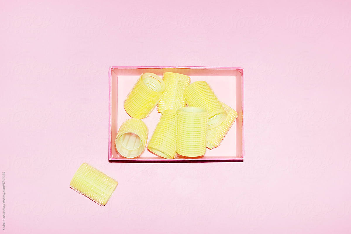 Neon yellow hair curlers on a pink background with hard flashlight