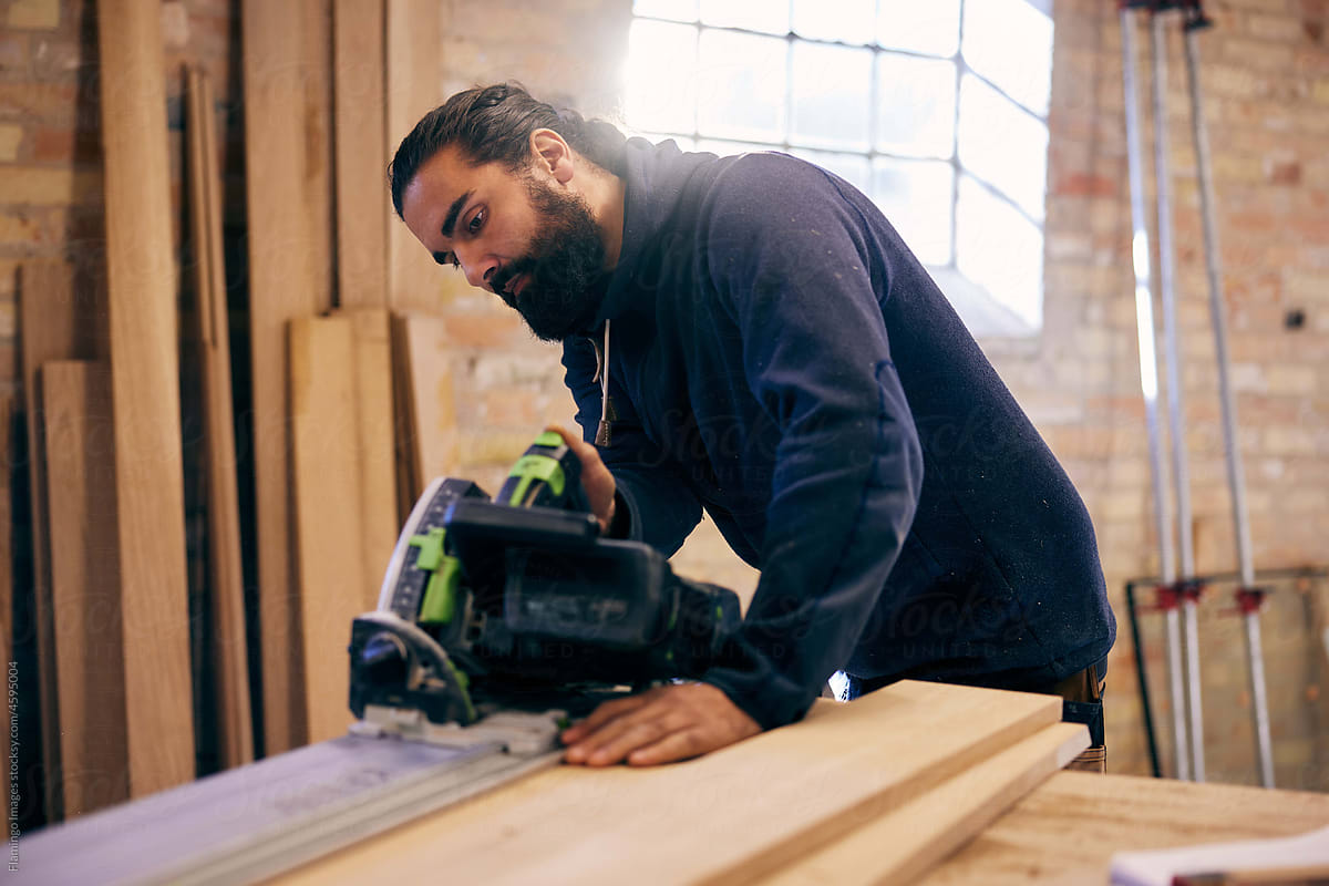 Woodworker sawing a plank at a bench in his workshop