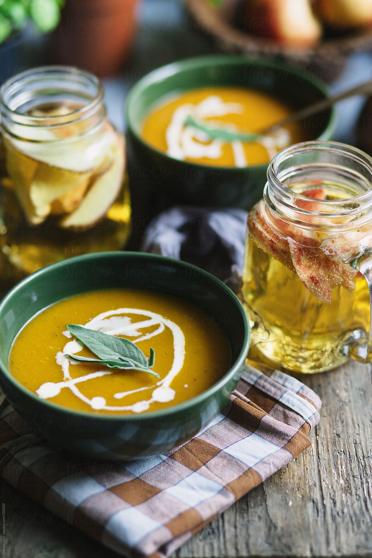 Two bowls of butternut squash soup and cider on a table.