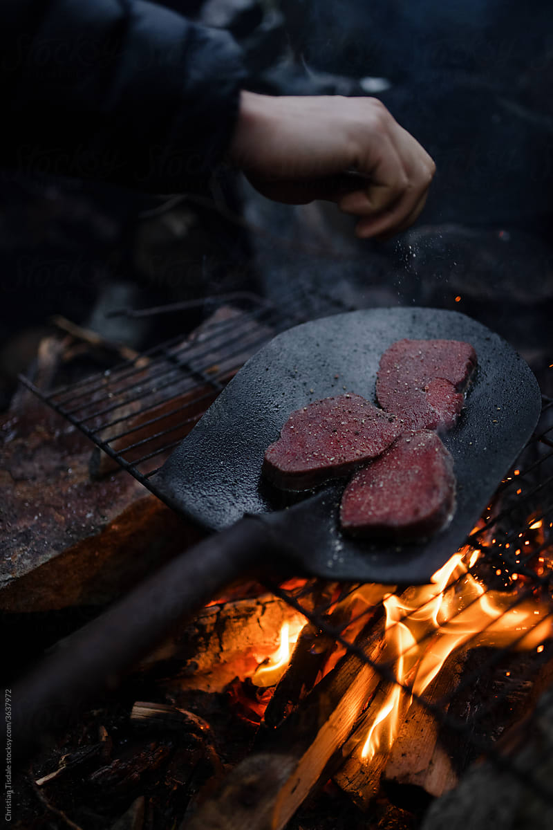 Steak being cooked over an open fire in a shovel