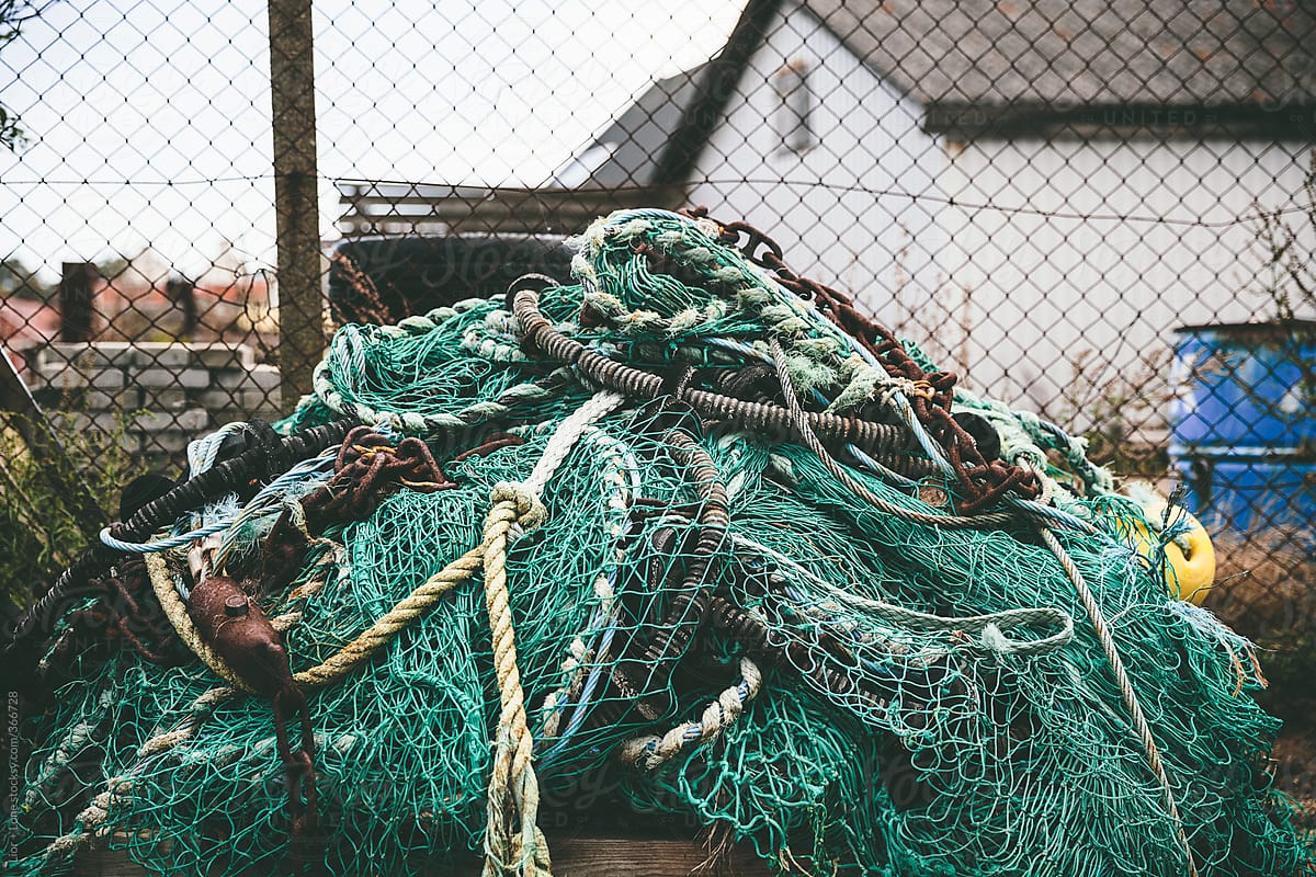 Pile of green fishing nets, ropes and chains by an old fence