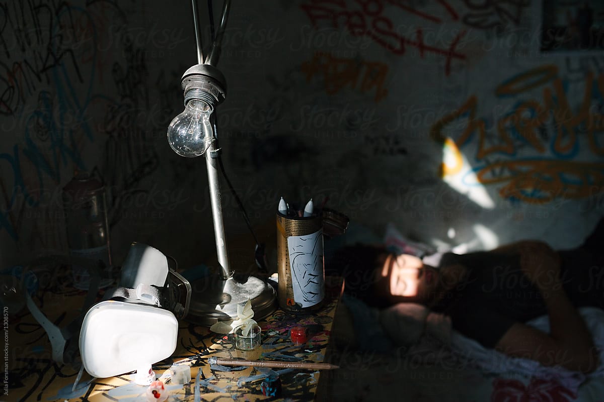 Desk of young graffiti artist with lamp, mask and spray paint.