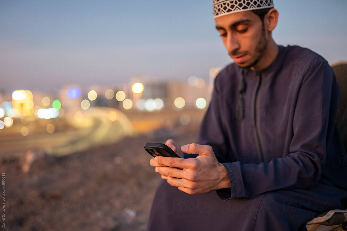 Focused Arab man browsing mobile while sitting on chair at sunset