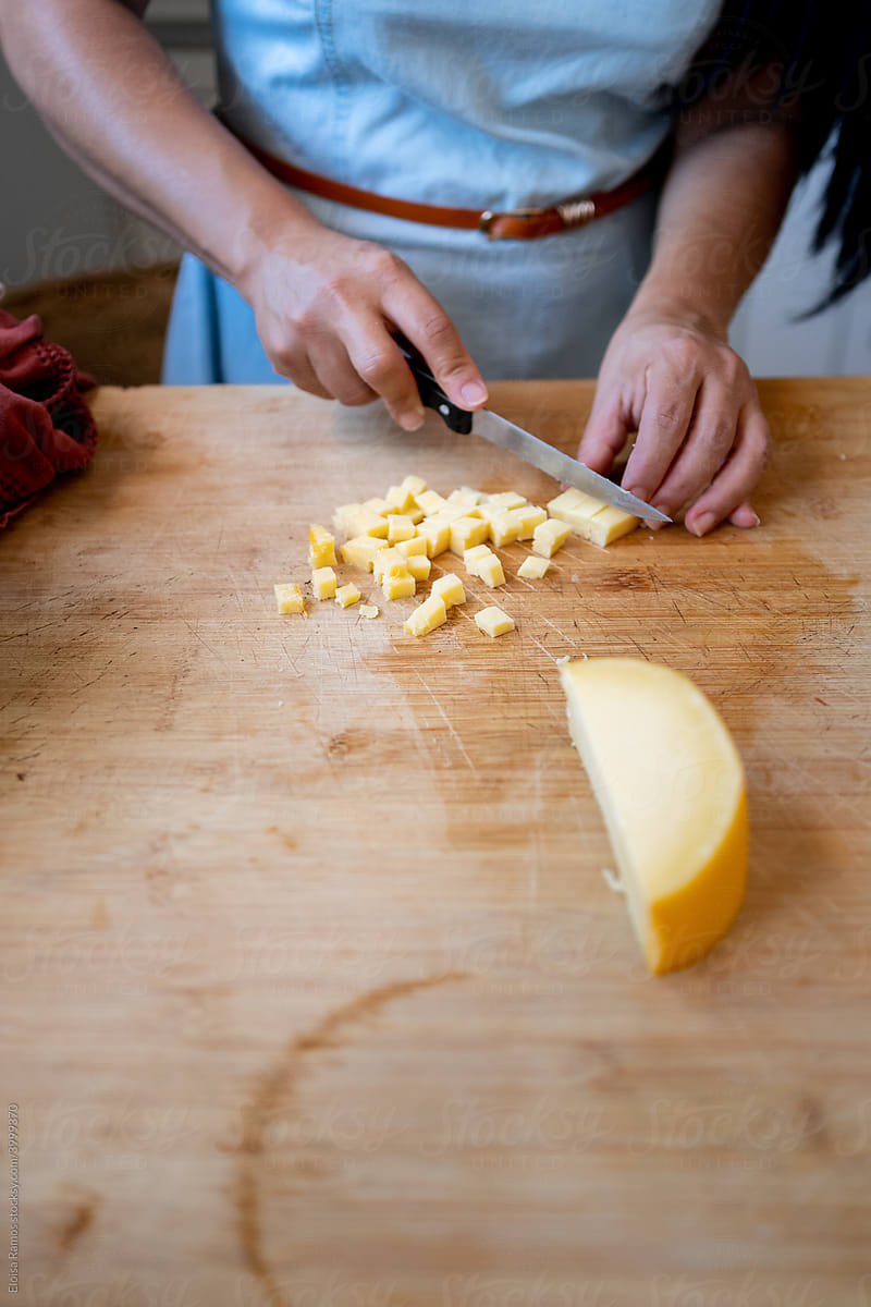 Detail of female arms dicing cheese on a cutting board