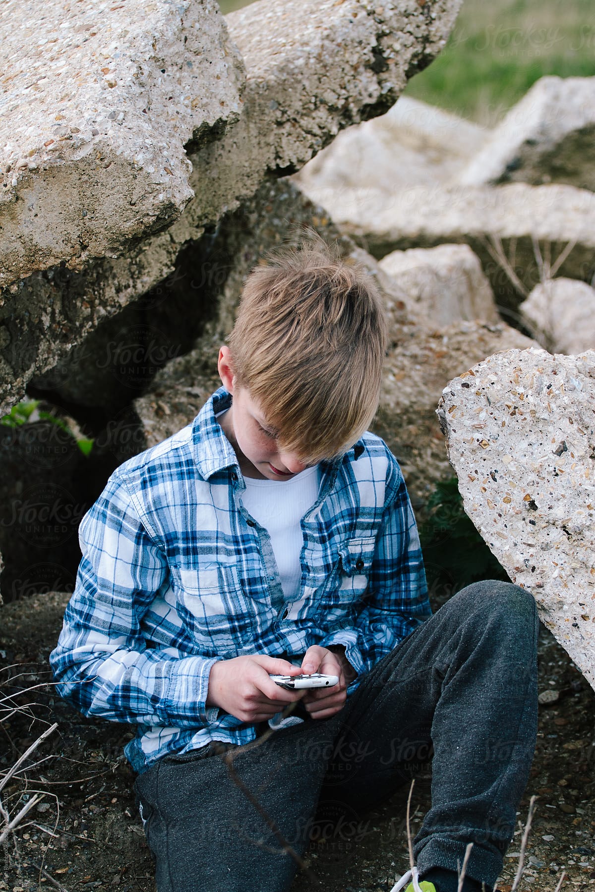 Trendy young boy sitting on a pile of rubble on waste ground. Texting.