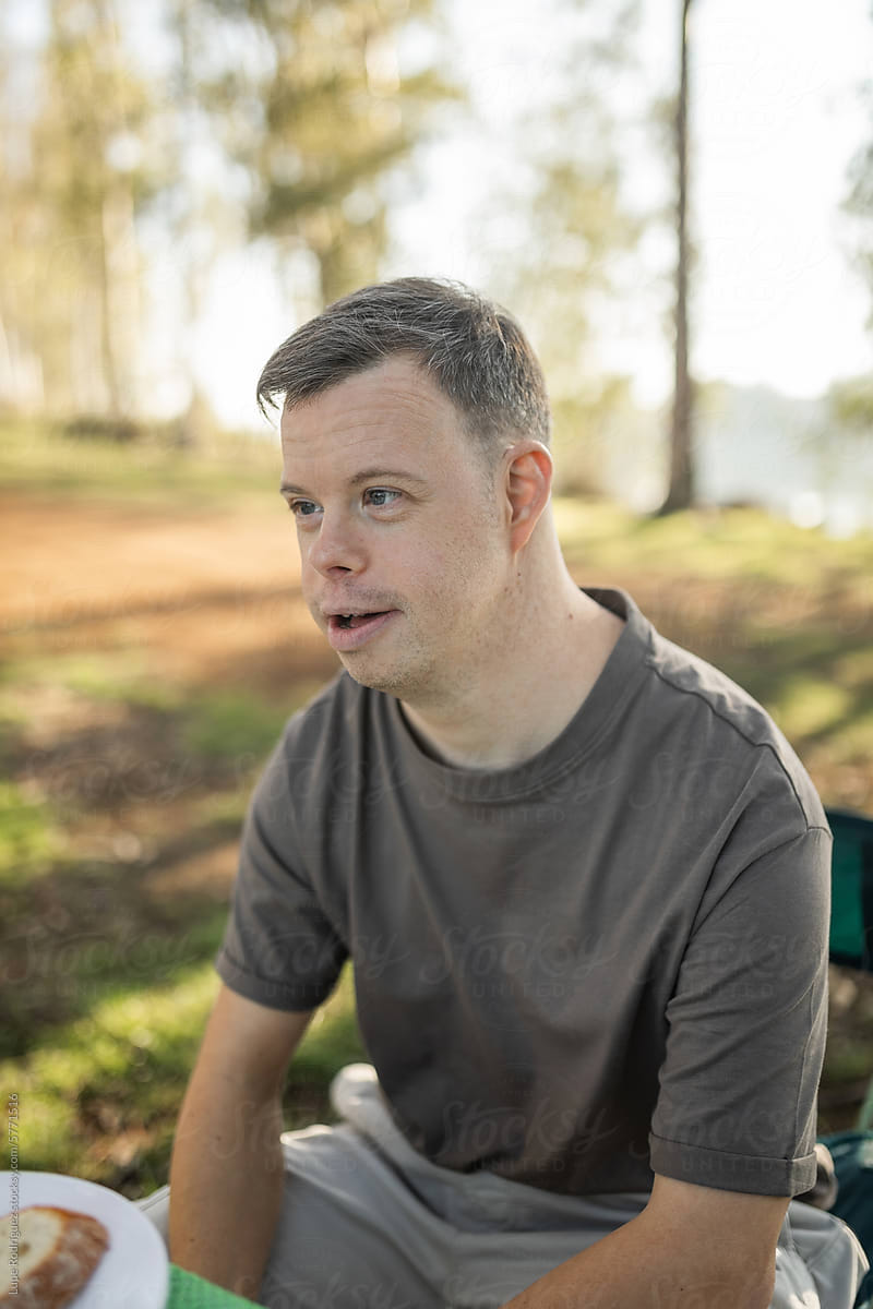 young man with down syndrome camping in nature having breakfast