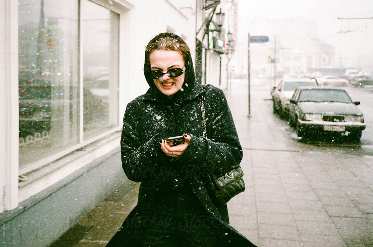 Girl checking her phone during a snowstorm in a retro style street