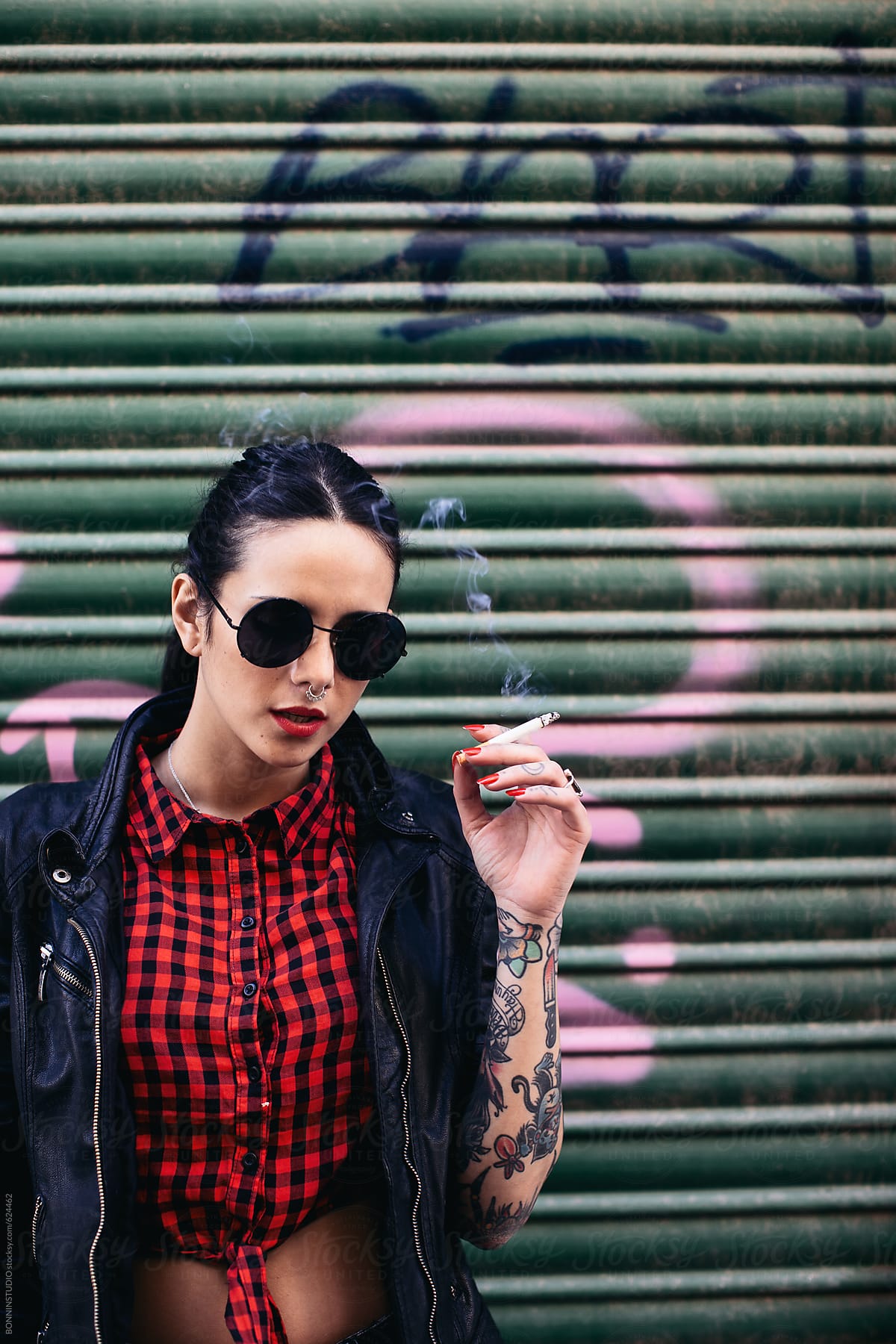 Portrait of a young alternative woman smoking in front a graffiti shutter door.