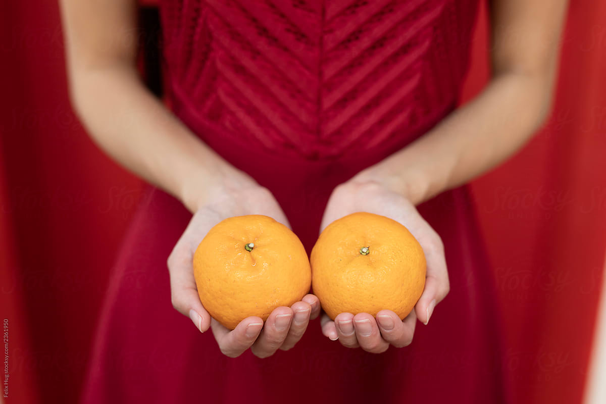 Chinese New Year, a detail shot of two female hands holding oranges in front of a red background