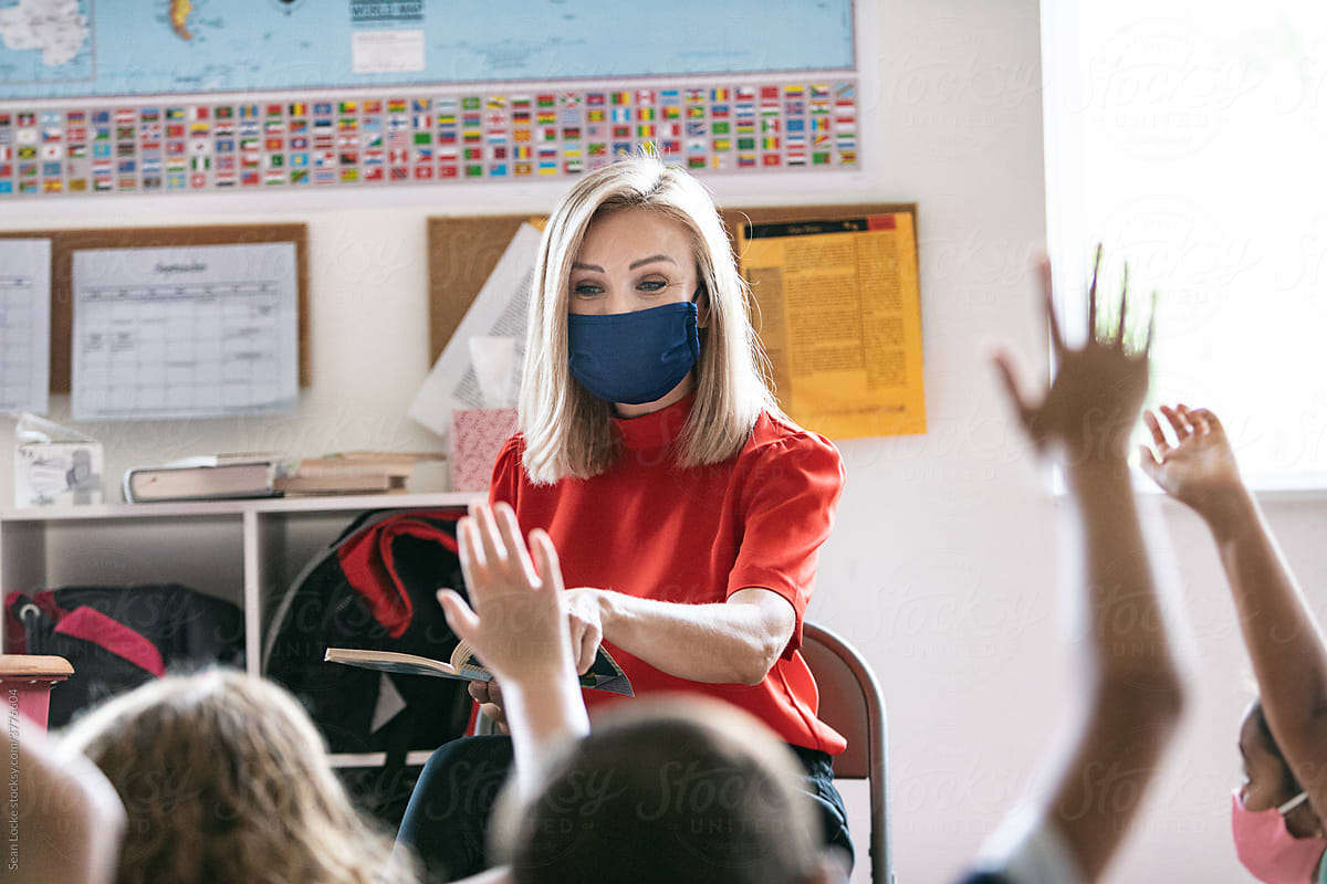 School: Teacher Wearing Face Mask And Reading Book Asks Question