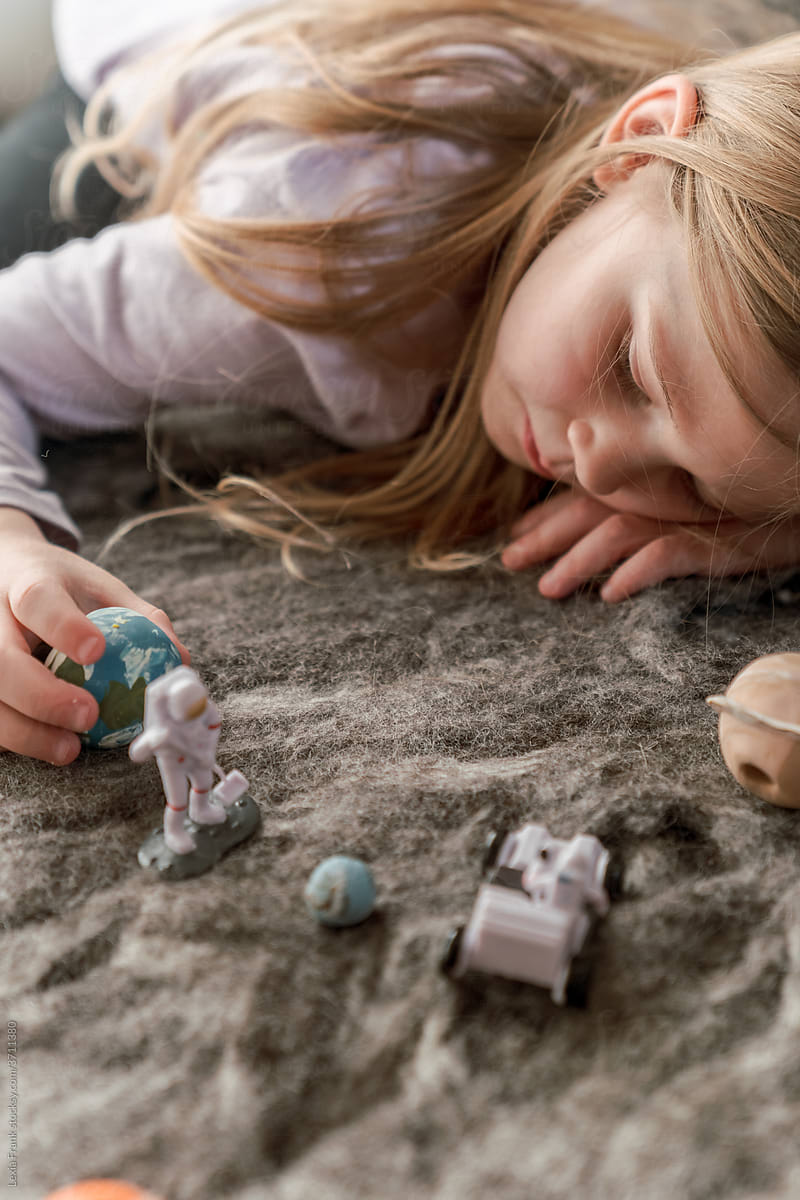little girl plays with space toys laying down