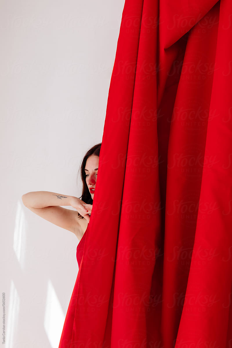 Young woman with black hair standing behind red curtain