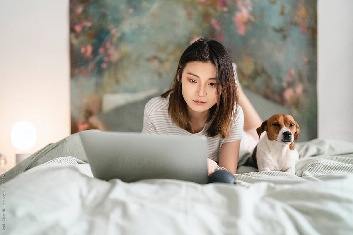 Woman working remotely on bed with dog