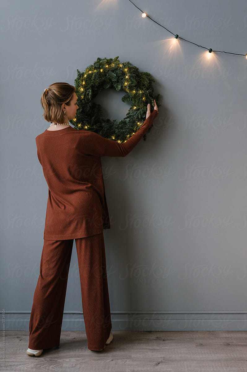 Woman hanging Christmas wreath on wall