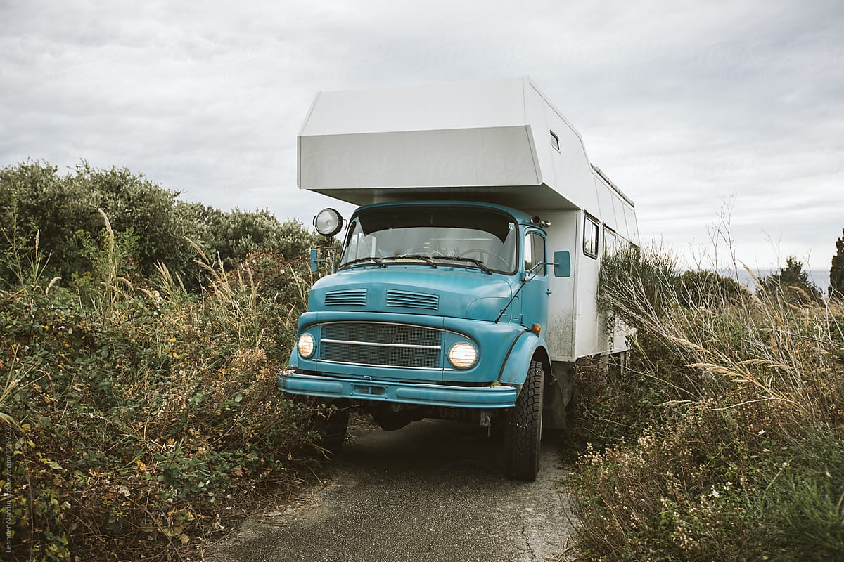 blue old camping truck on a tight and overgrown road