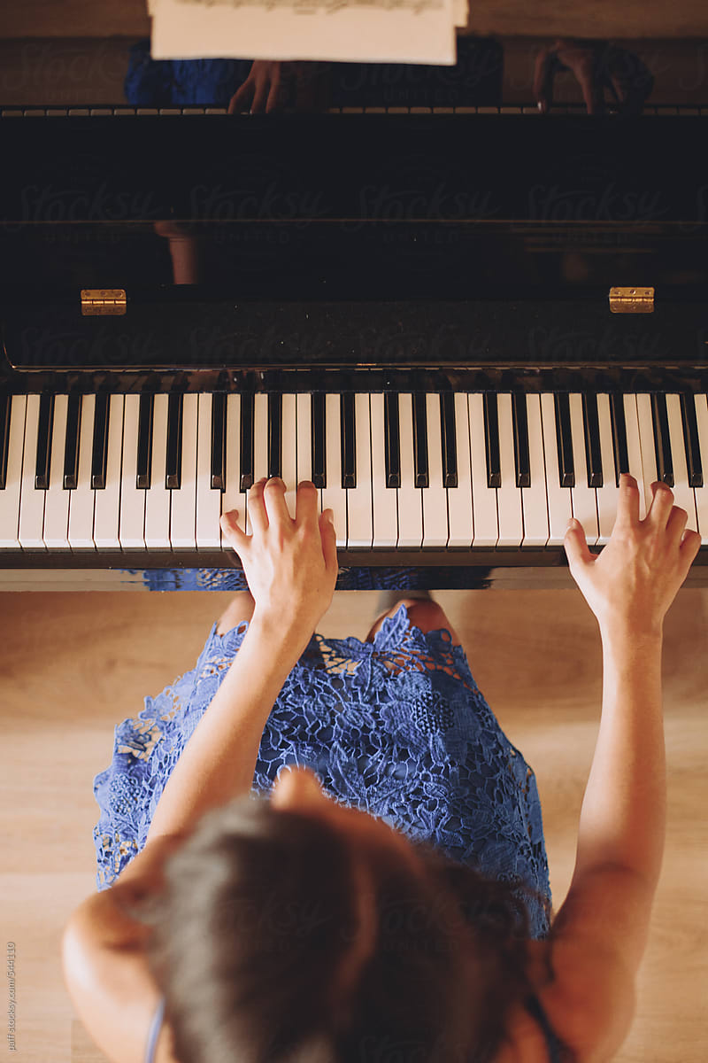 Picture from above of a young woman in blue dress playing the piano