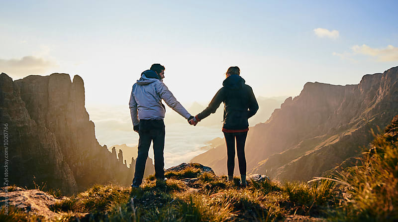 Young hiking couple holding hands enjoying the sunrise over an epic mountain valley.