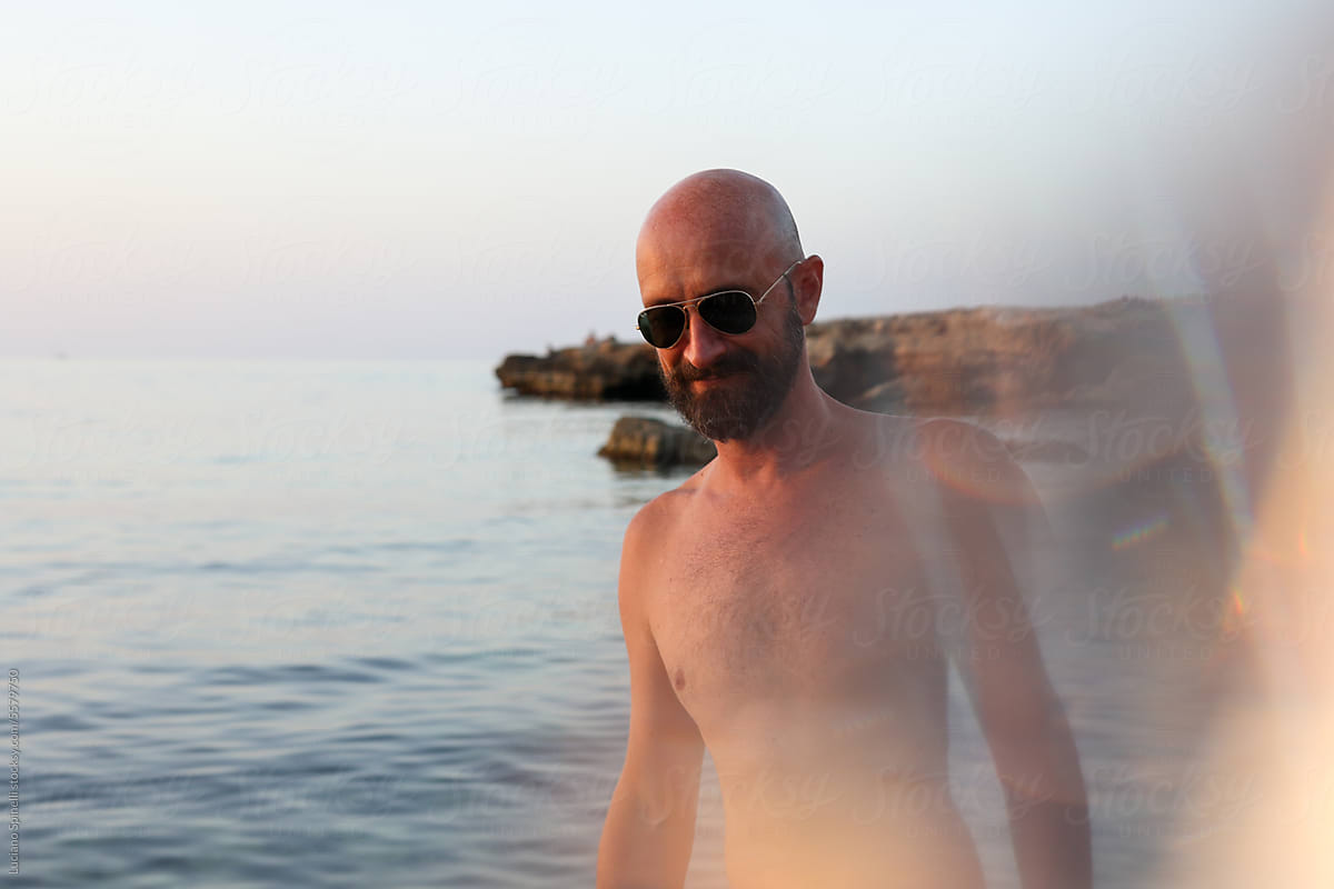Shirtless man walk by the rocky beach during sunset with light effect