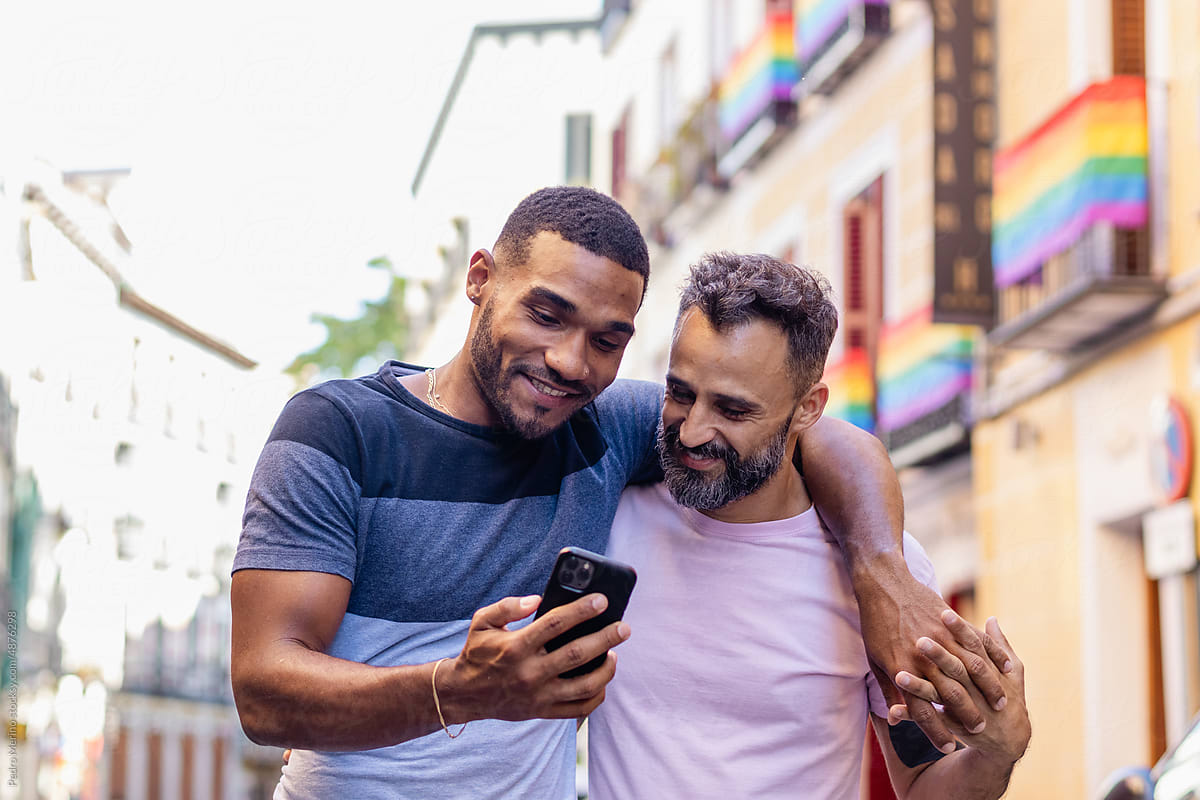 Gay couple walking down the street holding each other using smartphone