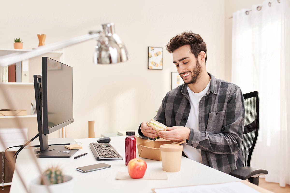 Happy busy man with healthy takeaway food at workplace