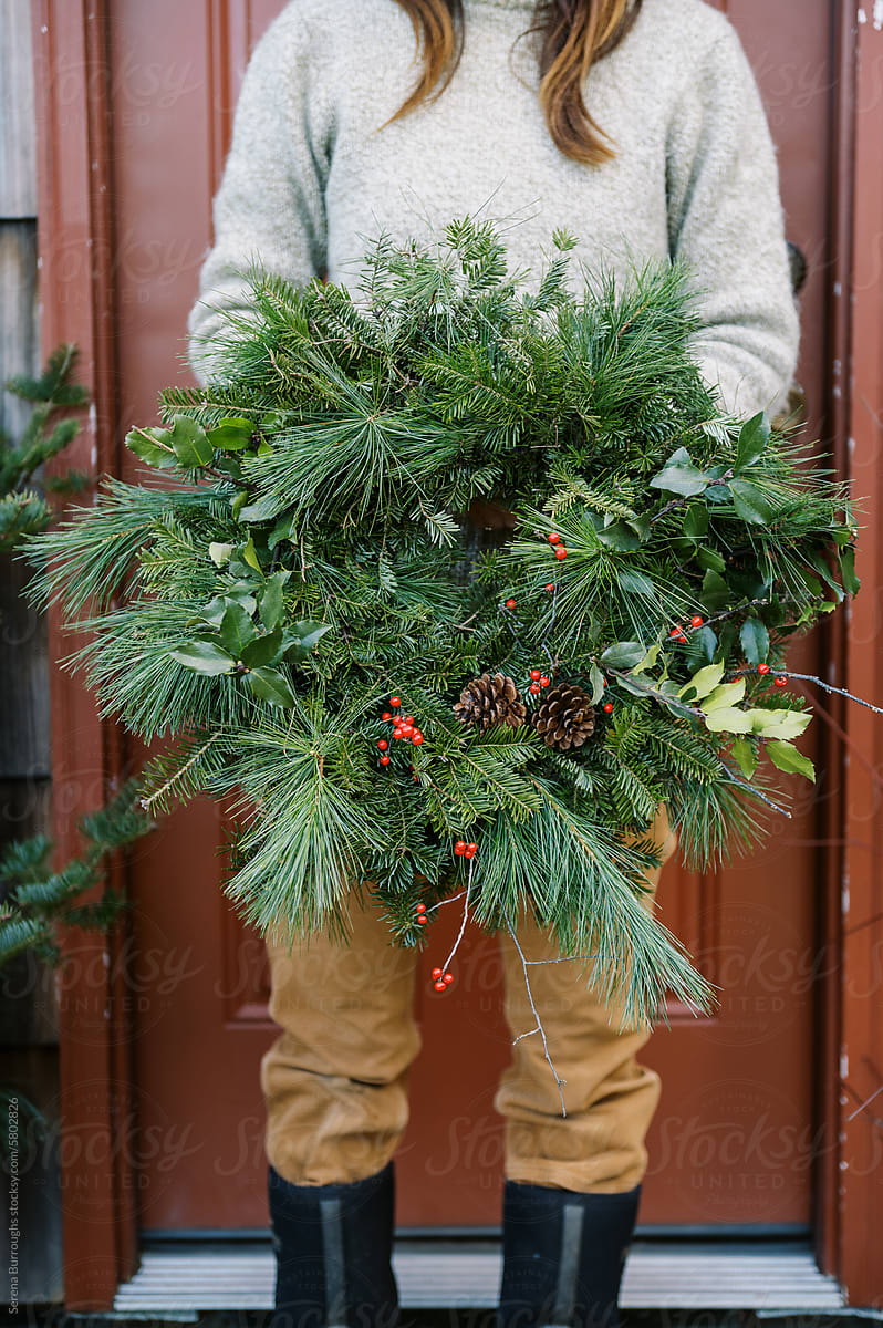 farmer holding holiday wreath in front of red door
