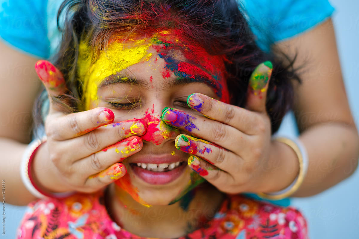 Mother smearing color powder on her daughters face during holi celebration,portrait