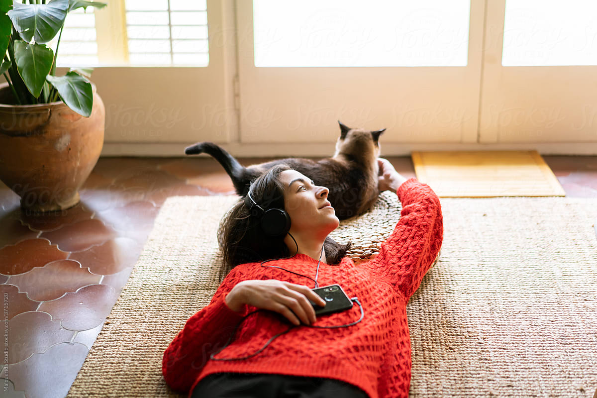 Woman with headphones lying on the floor with her cat