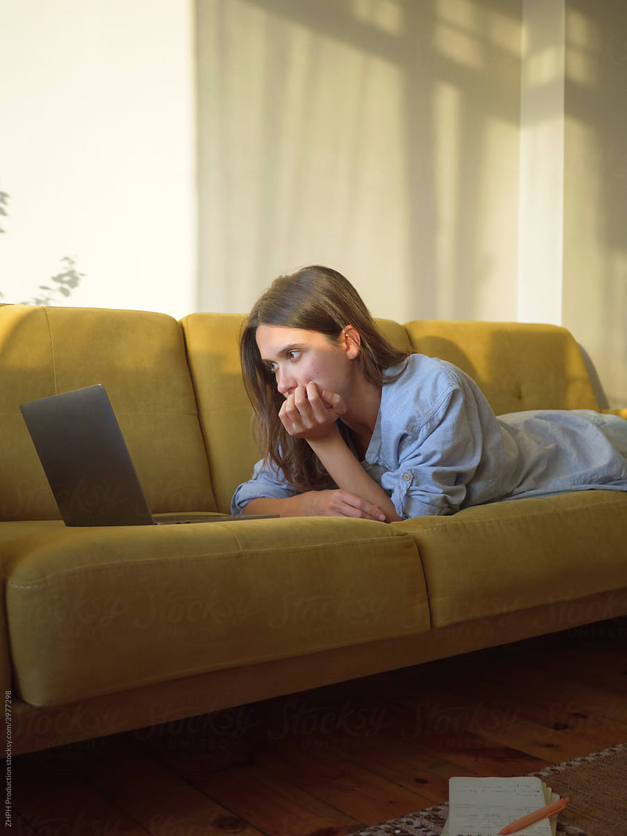 Woman with laptop and notebook laying on sofa at home study homework